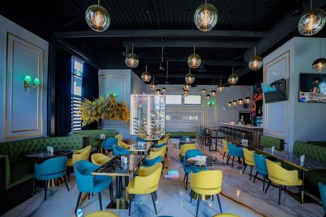 Interior of a restaurant with teal and yellow chairs, marble floor, and glass globe lights.