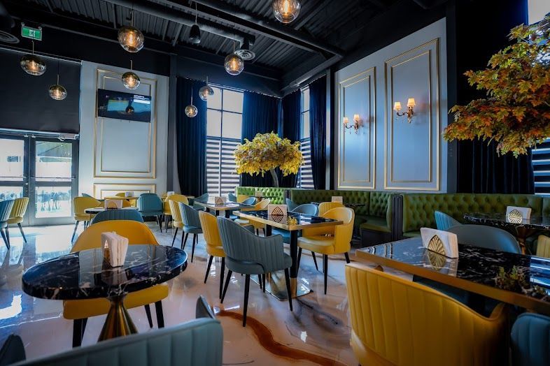 Elegant restaurant interior with yellow and blue chairs, marble tables, and ornate wall panels.