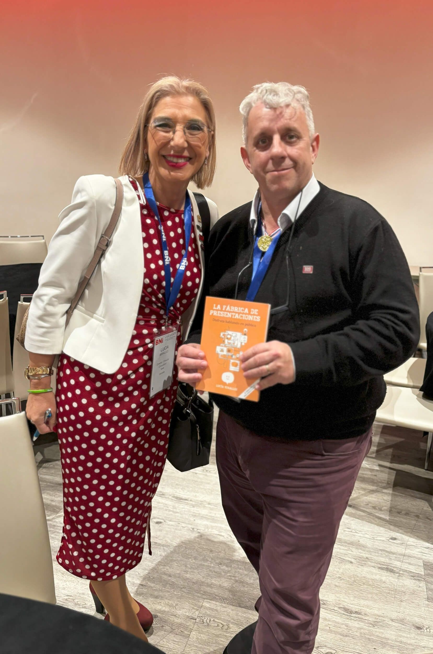 Mujer con lunares y hombre con libro sonriendo juntos en el interior.