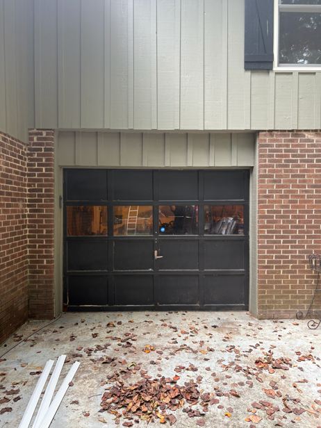 Garage door on a house with brick and siding, covered with fall leaves on the ground.