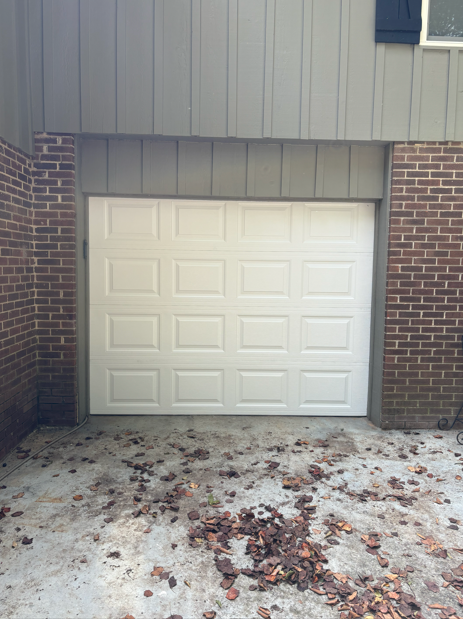 White garage door in a brick and gray-paneled exterior. Leaves are scattered on the concrete driveway.