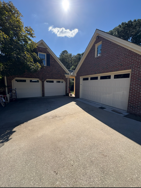 Two brick garages with white doors, connected by a pathway, set in sunlight against a blue sky.