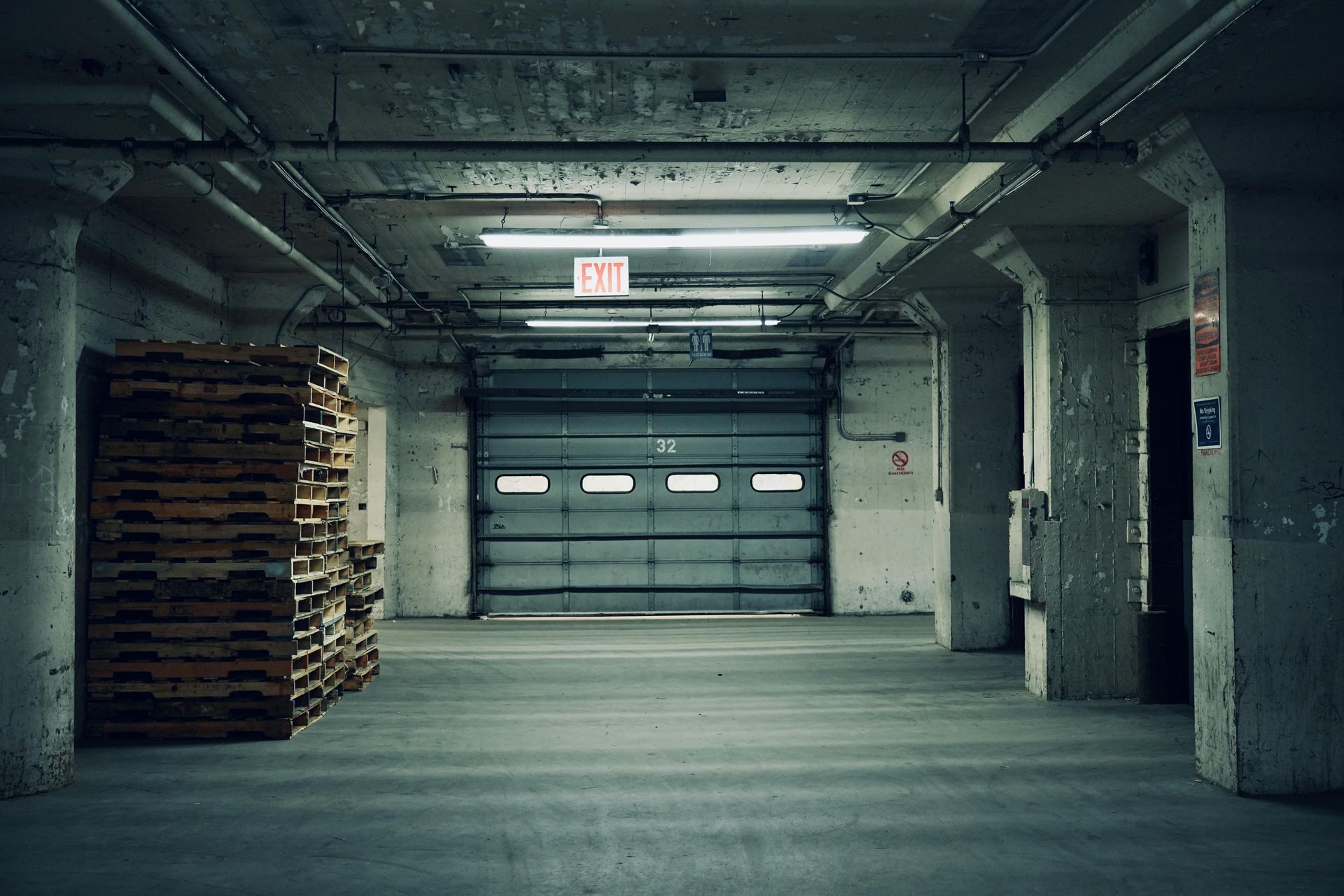 Gritty warehouse interior with loading dock, pallets, and overhead lighting.