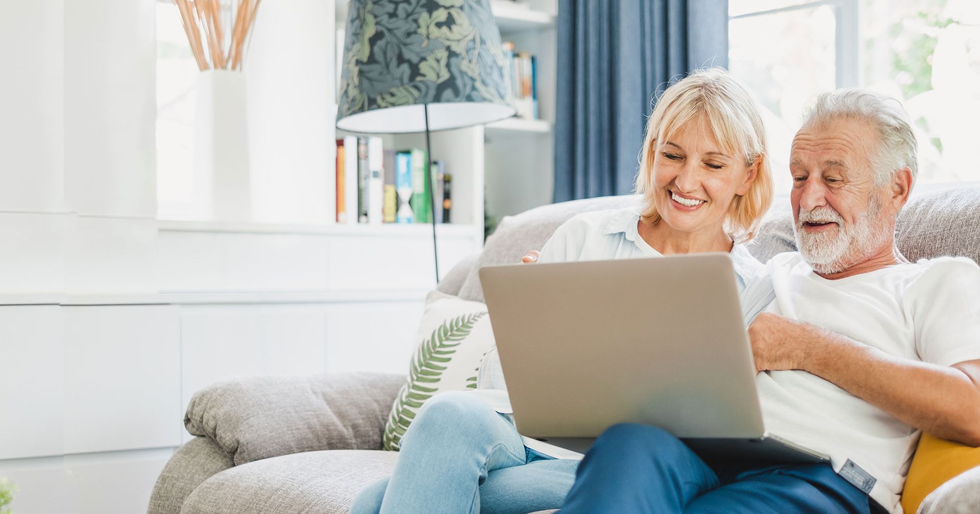 An elderly couple is sitting on a couch using a laptop computer.