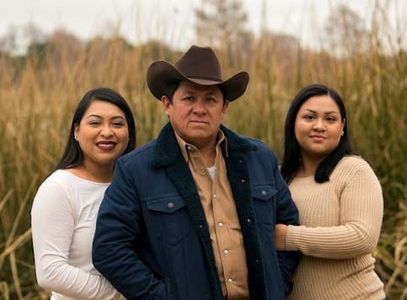 A man in a cowboy hat is standing next to two women in a field.