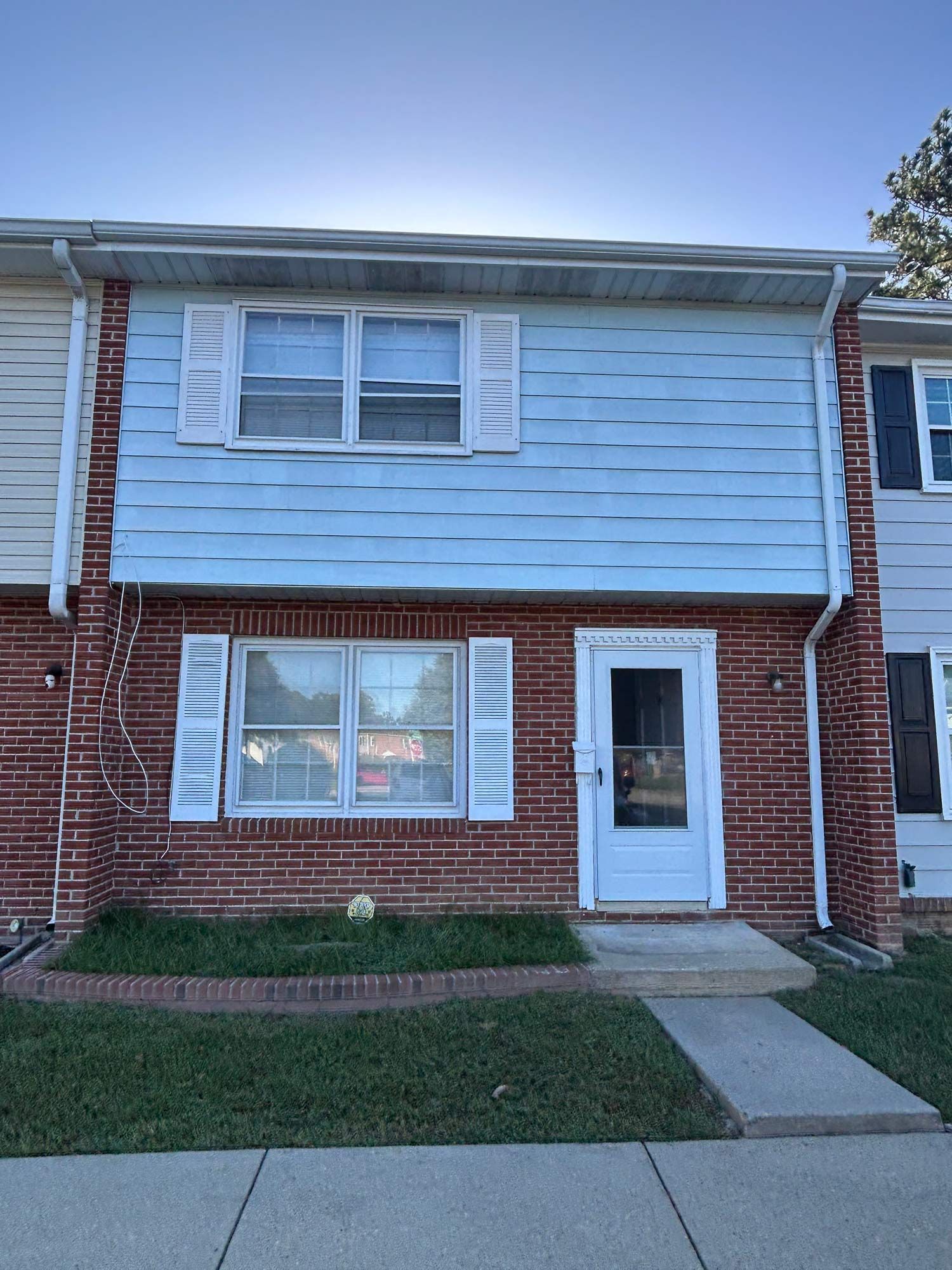 Two-story townhouse with red brick base, blue siding above, white shutters, and a front door.