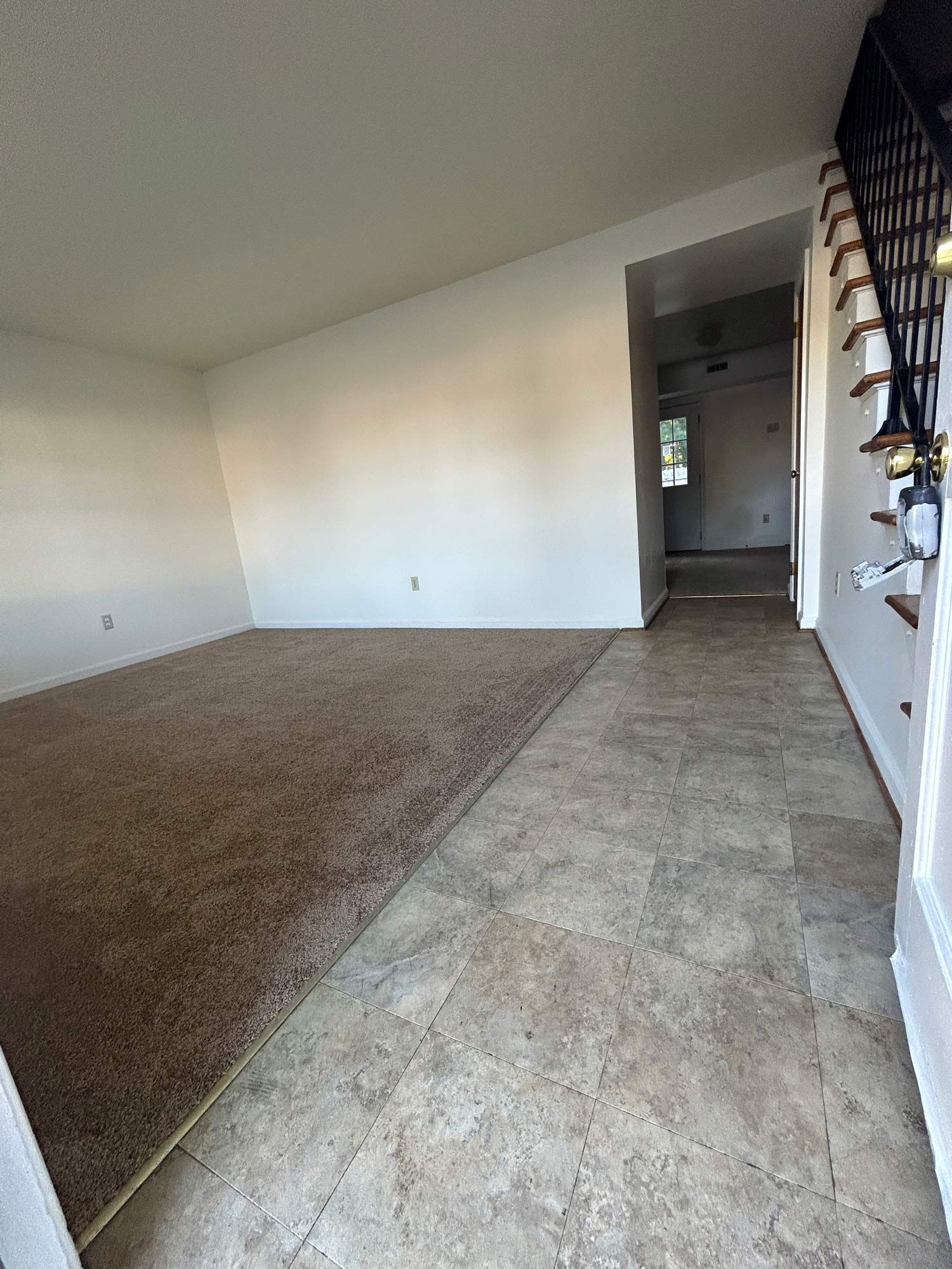 Entryway with carpet and tile flooring leading to a hallway and stairs. White walls, neutral tones.