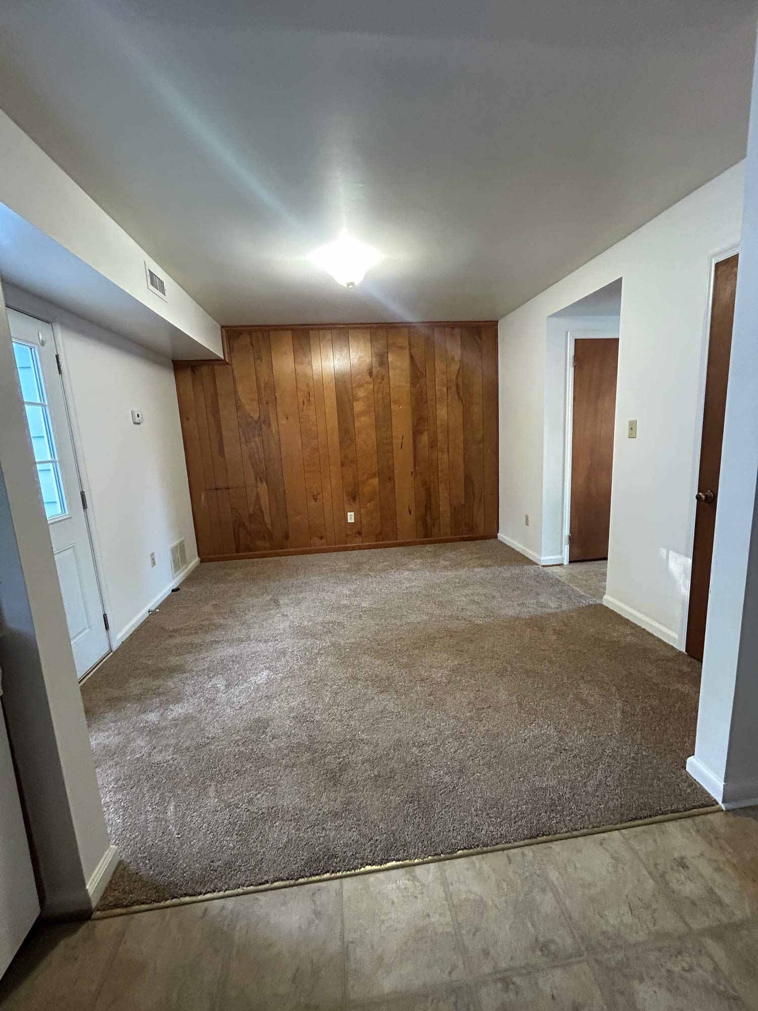 Empty room with brown carpet, wood-paneled wall, white walls, and two doorways.