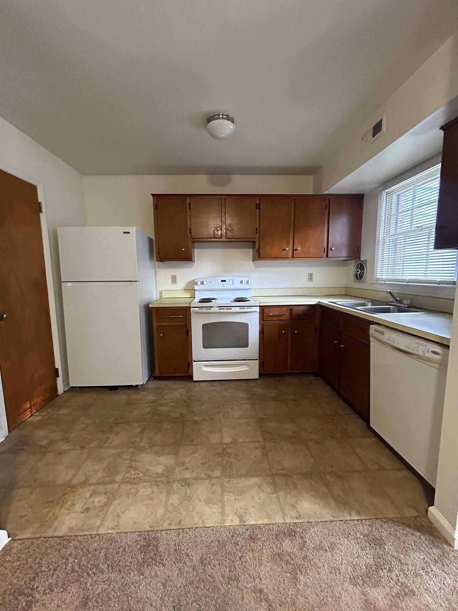 Kitchen with brown cabinets, white appliances, and linoleum flooring.