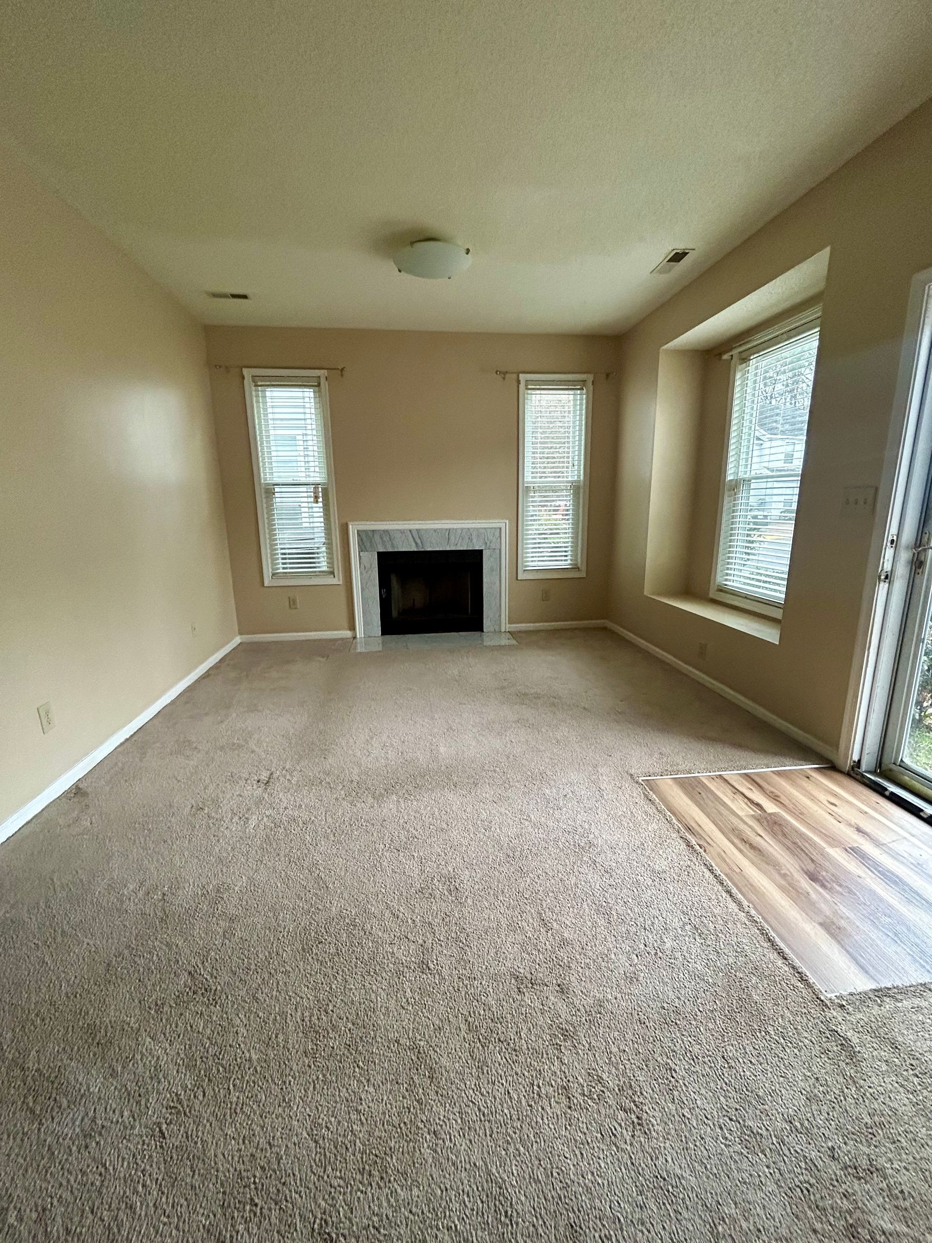 Empty living room with fireplace, windows, and brown carpet.