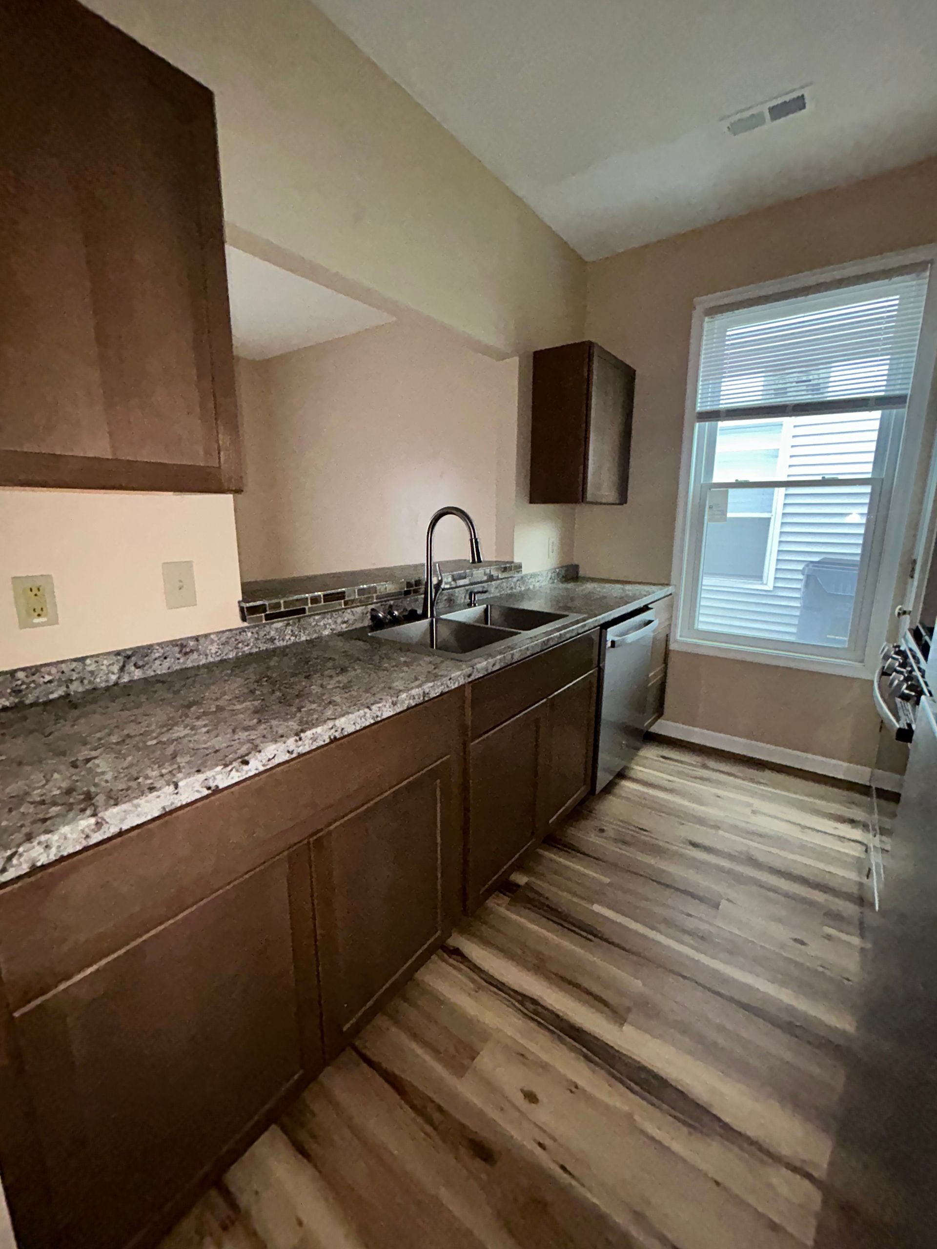 Kitchen with brown cabinets, gray countertops, sink, and window with blinds.