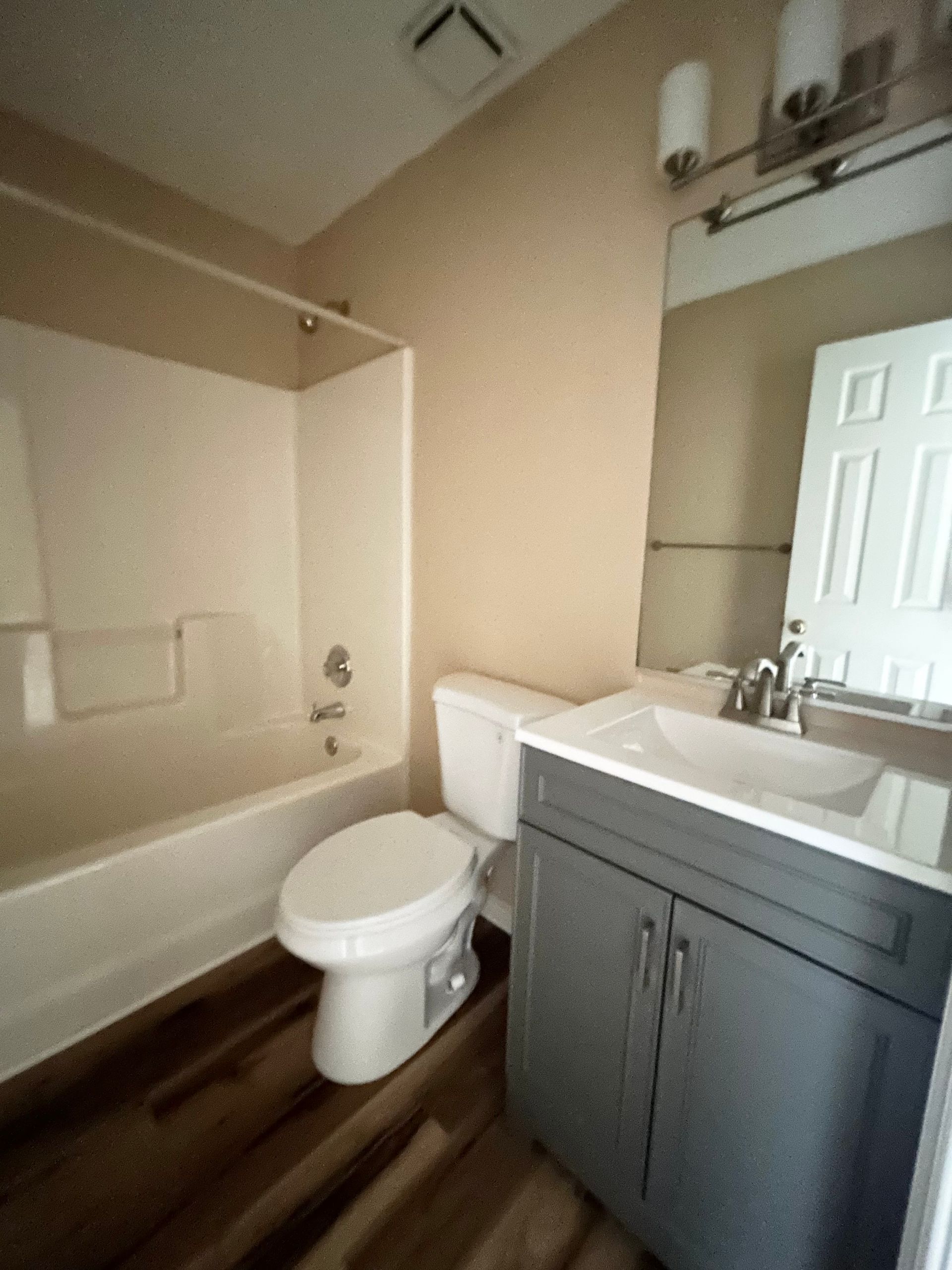 Bathroom with a white tub, toilet, gray vanity, and wood-look flooring.