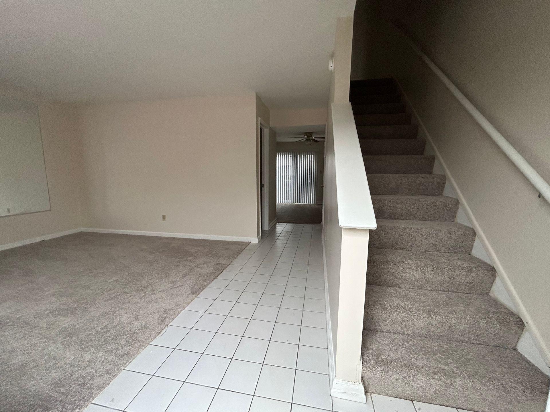 An interior view showing a carpeted living area, a tiled entryway, and a carpeted staircase with a white railing.