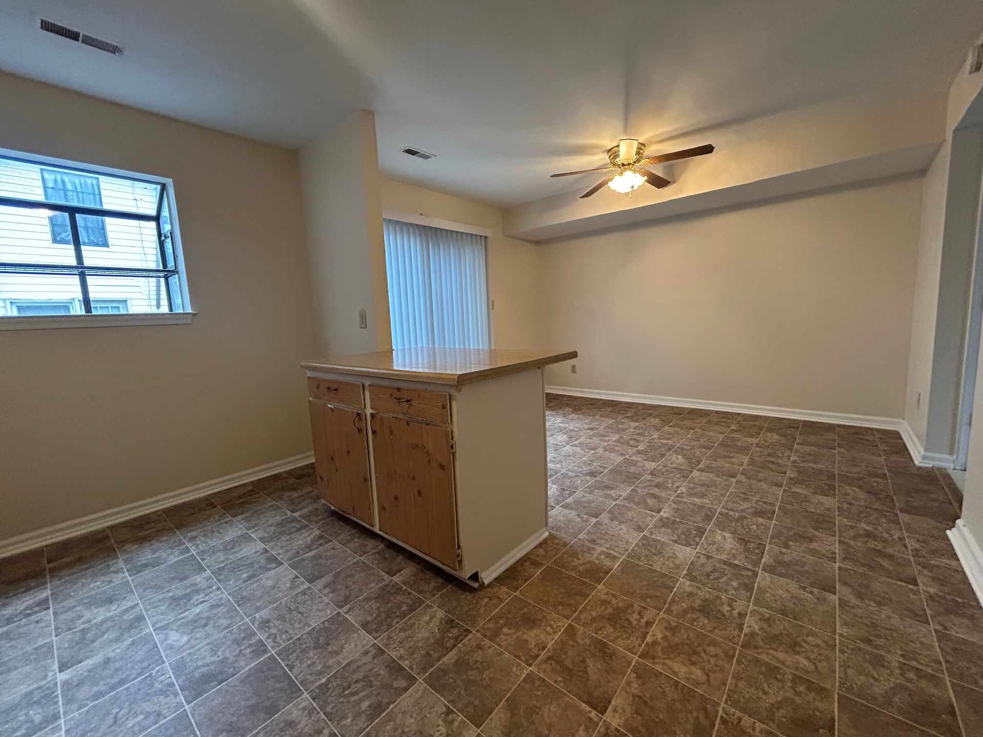 An empty, open-concept kitchen and living area with tan walls, brown patterned tile flooring, and a central island.