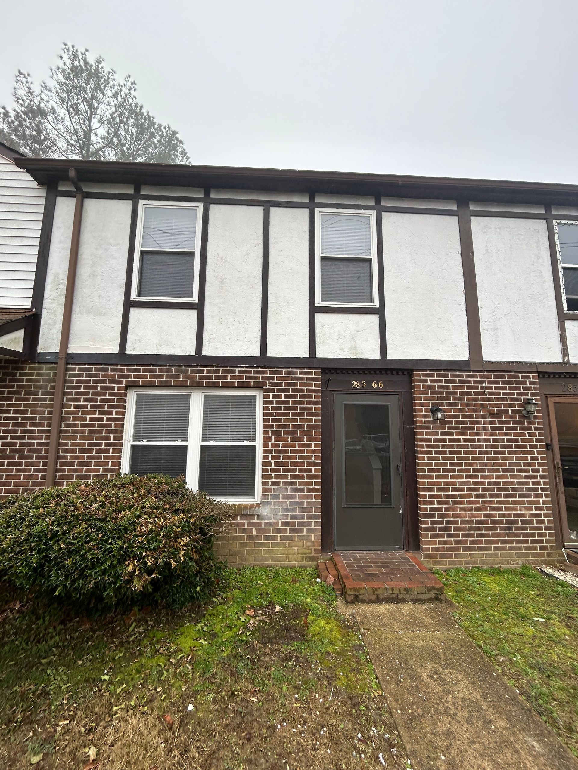 A two-story townhouse with a brown brick lower level, a white stucco and timber upper level, and a central front door.
