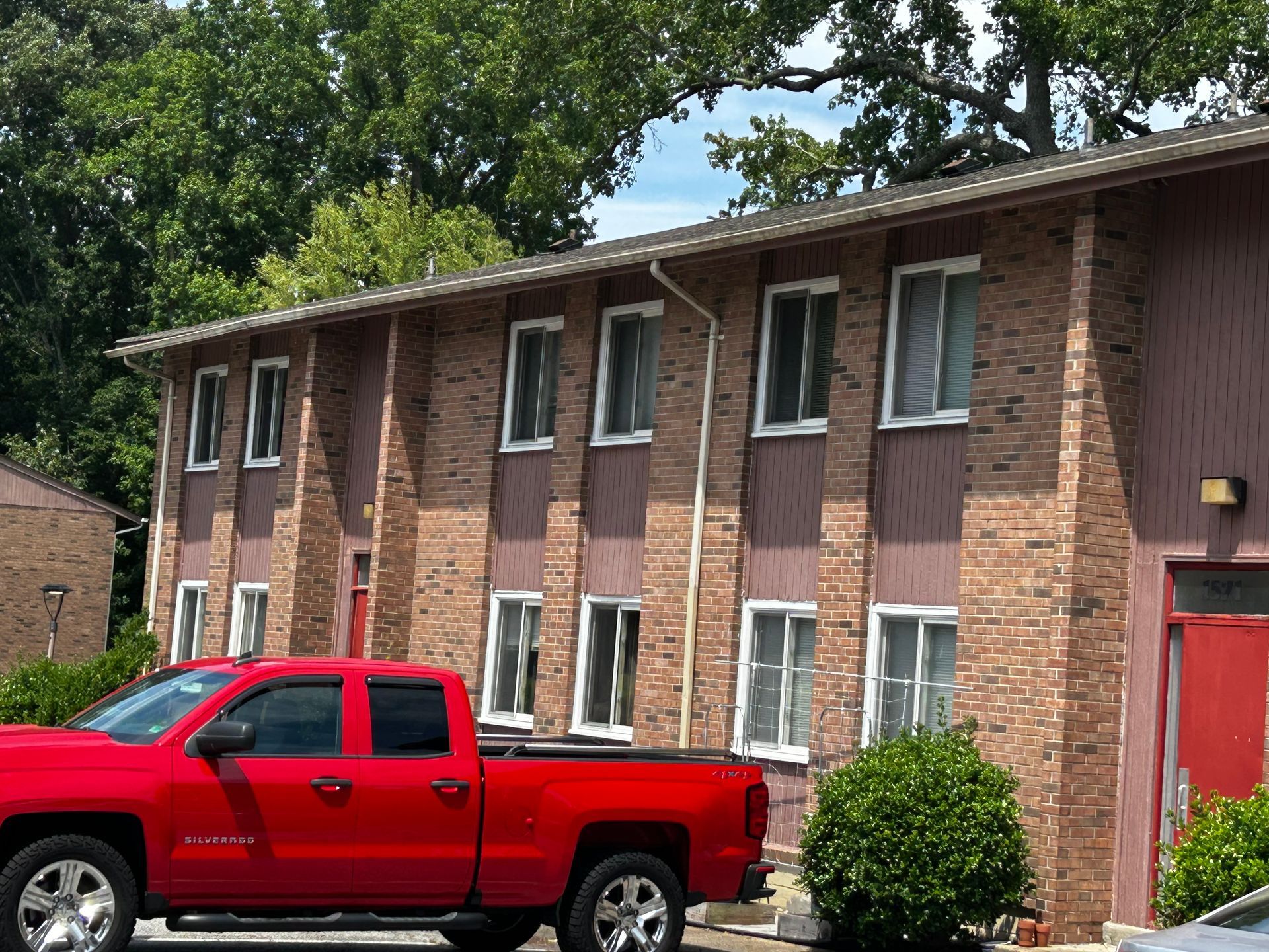 Red pickup truck parked in front of a brick apartment building with white-trimmed windows.