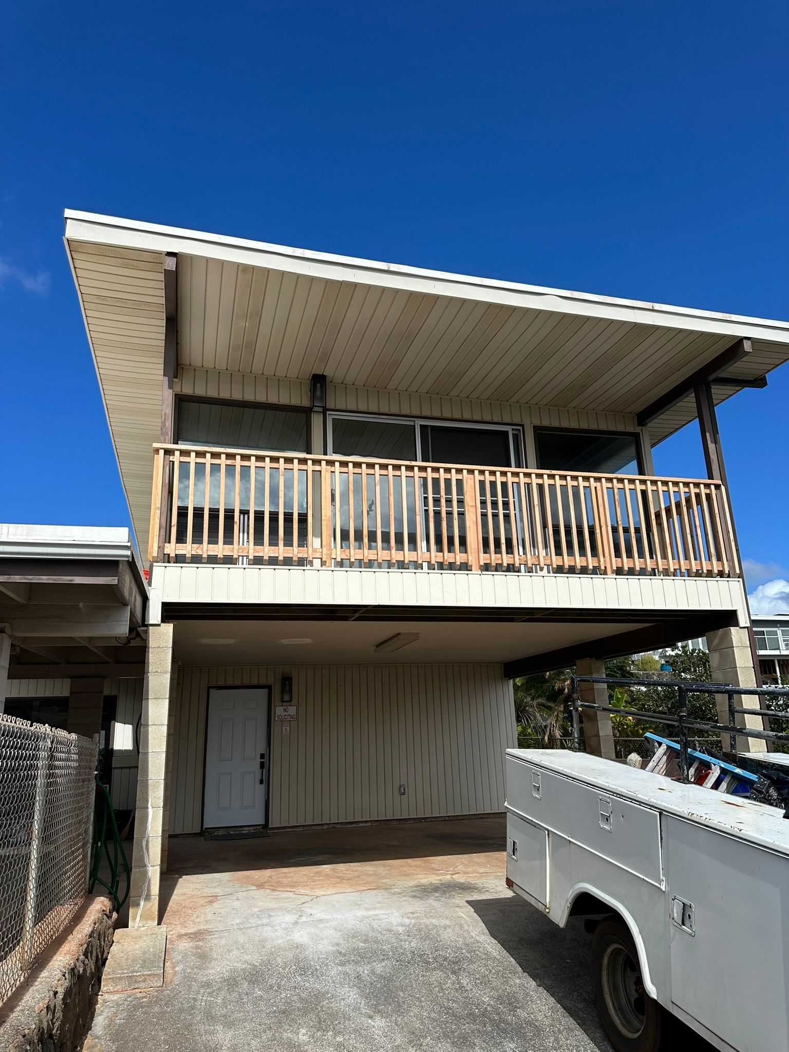 Two-story house with a balcony. White exterior, clear blue sky. A white utility truck is parked nearby.