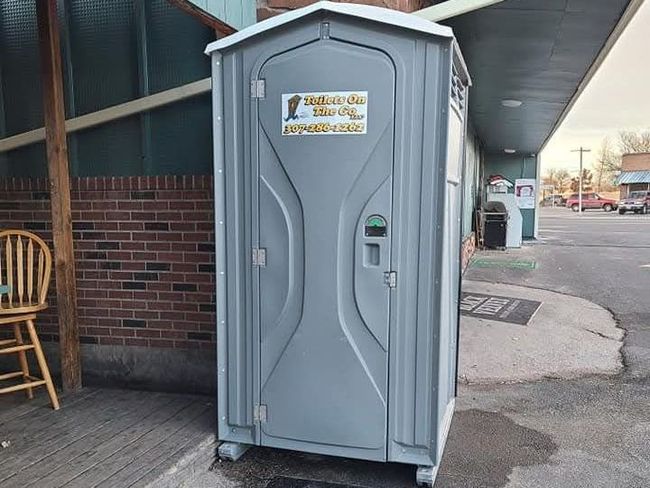 A Portable Toilet is Sitting in Front of a Brick Building | Cheyenne, WY | Toilets On The Go, LLC