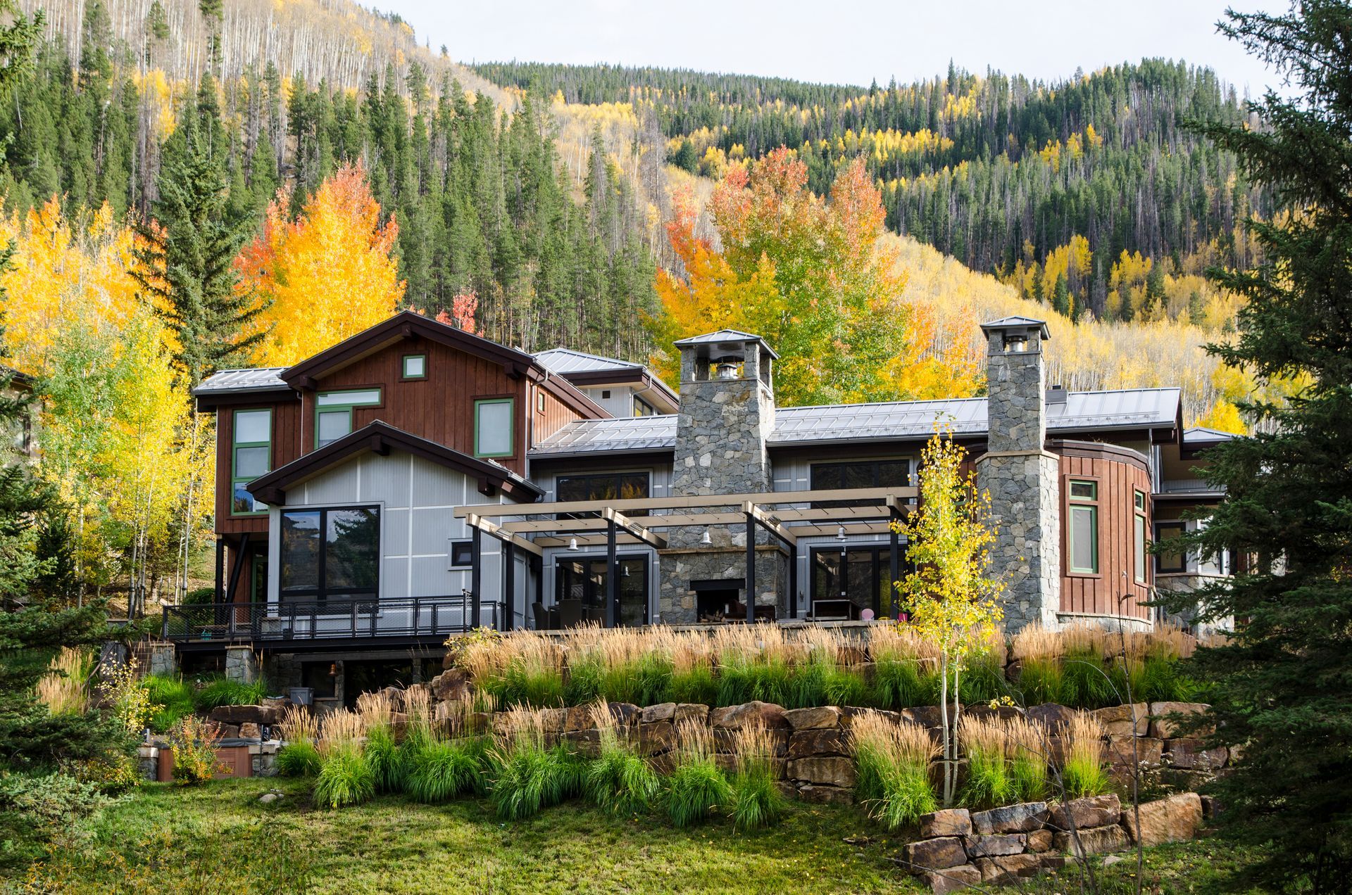Large mountain home surrounded by autumn trees; exterior view of the house with two stone chimneys.