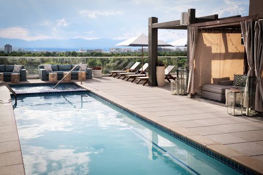 Rooftop pool with seating areas, cabana, and mountain views under a blue sky.