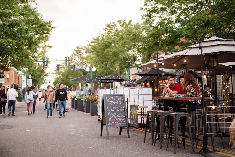 People walking along a street lined with outdoor dining, awnings, and trees.