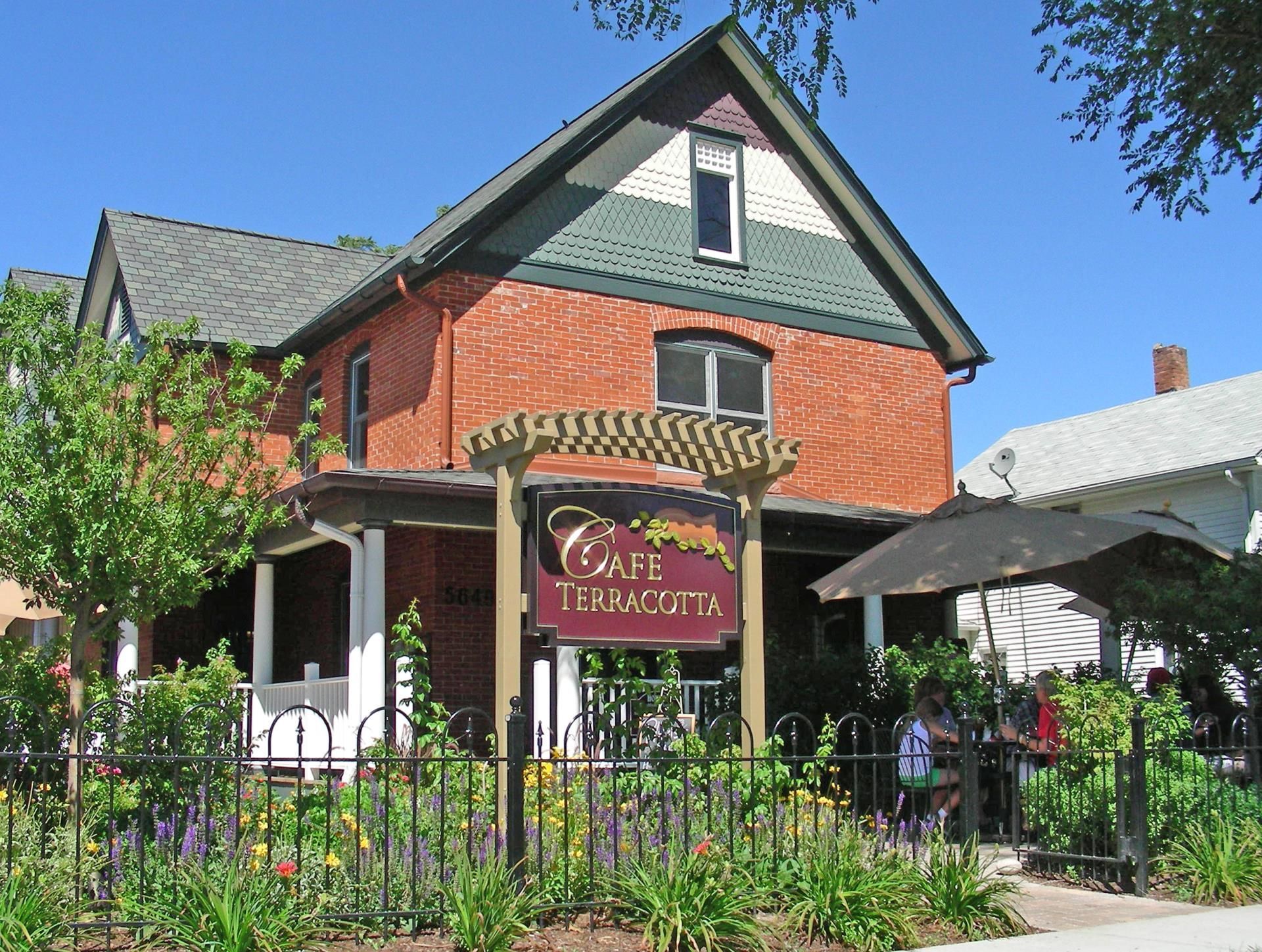 Cafe Terramotta storefront: brick building with sign, pergola, and a wrought-iron fence, with people at the entrance.