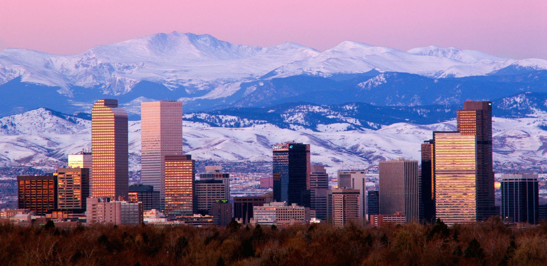 Denver skyline with snow-covered mountains in the background at sunset.