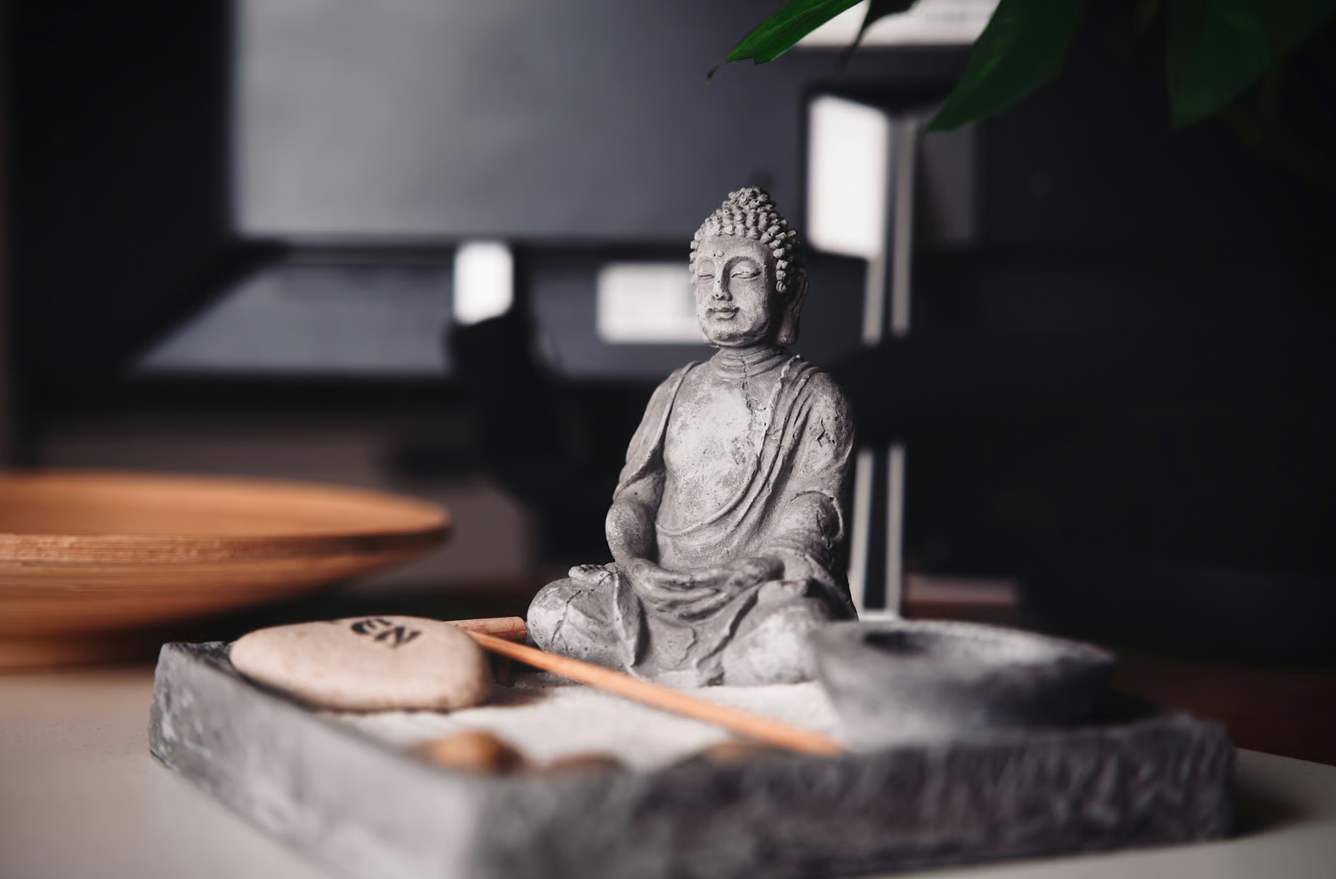 Stone Buddha statue on a small sand garden with a wooden rake.