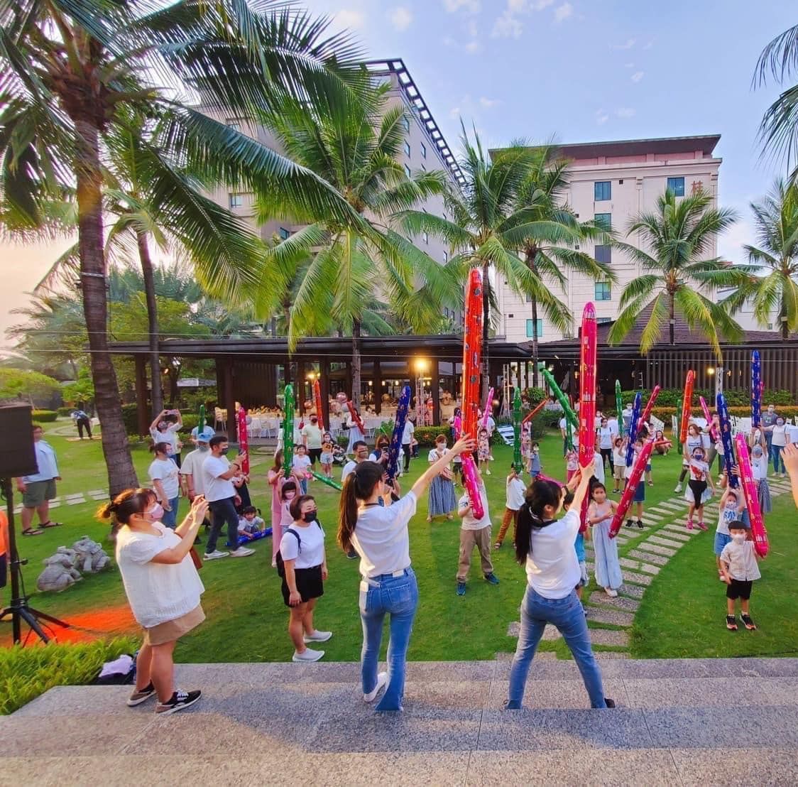 A group of people are dancing in a park with palm trees in the background