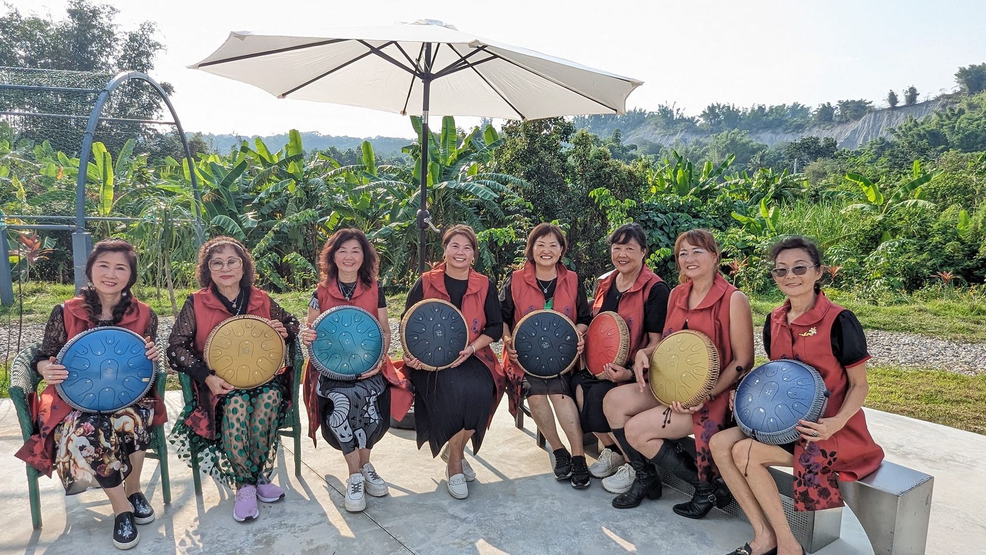 A group of women are sitting under an umbrella holding plates.
