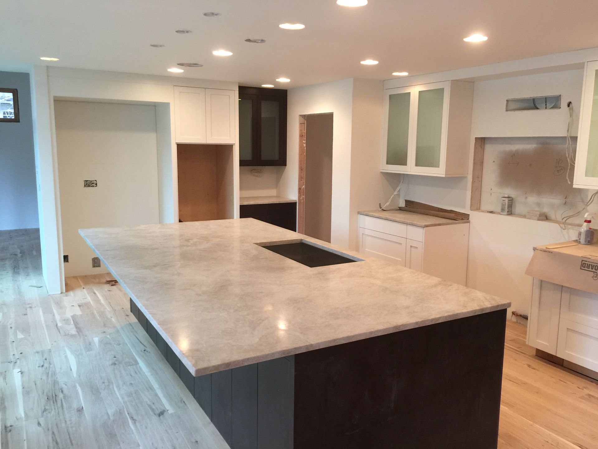 A kitchen with a large Marble Island with white cabinets