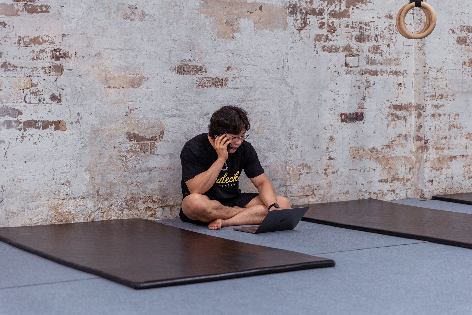 Image of a guy using his laptop and his phone in the gym