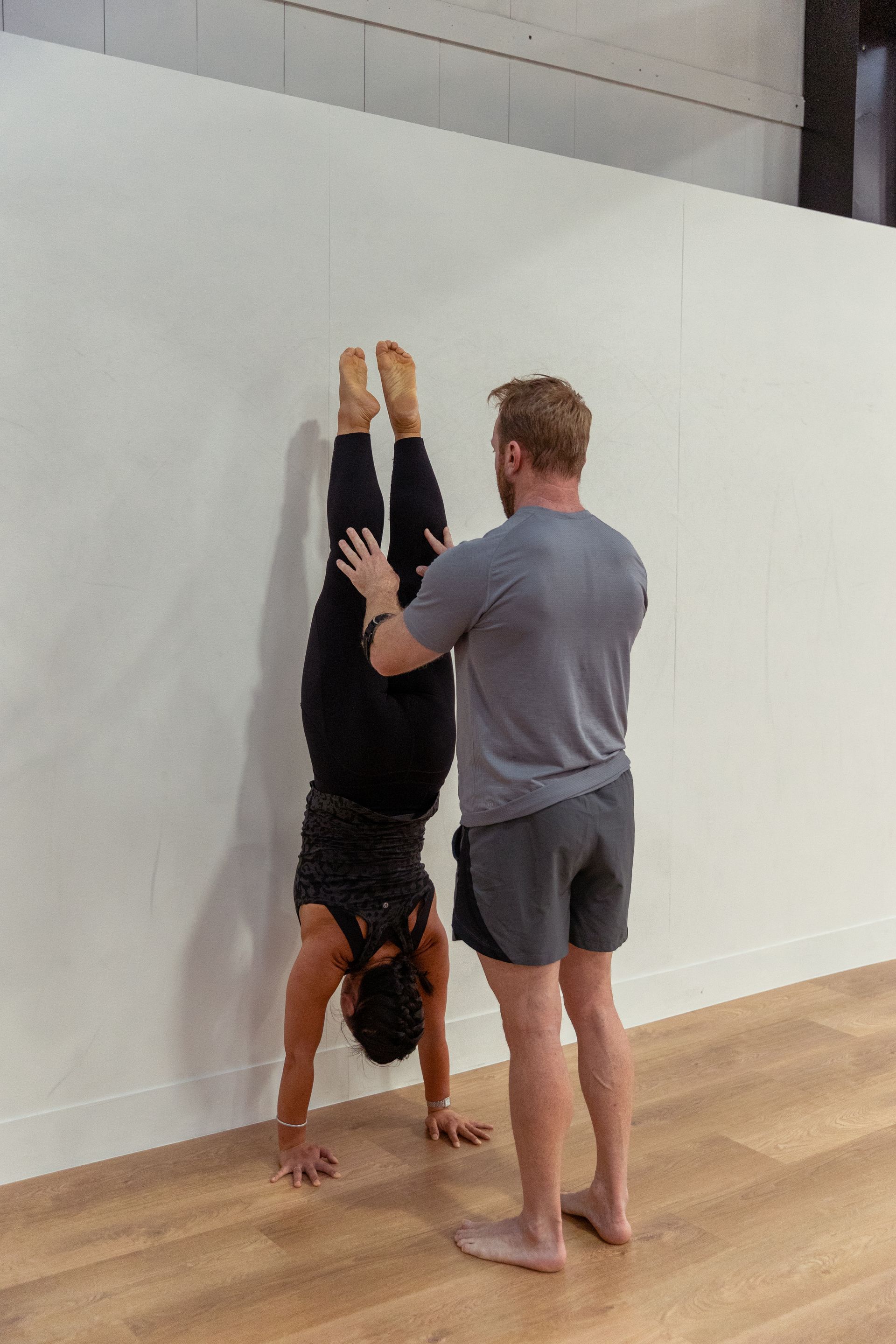 Image of a guy helping a woman in doing a handstand