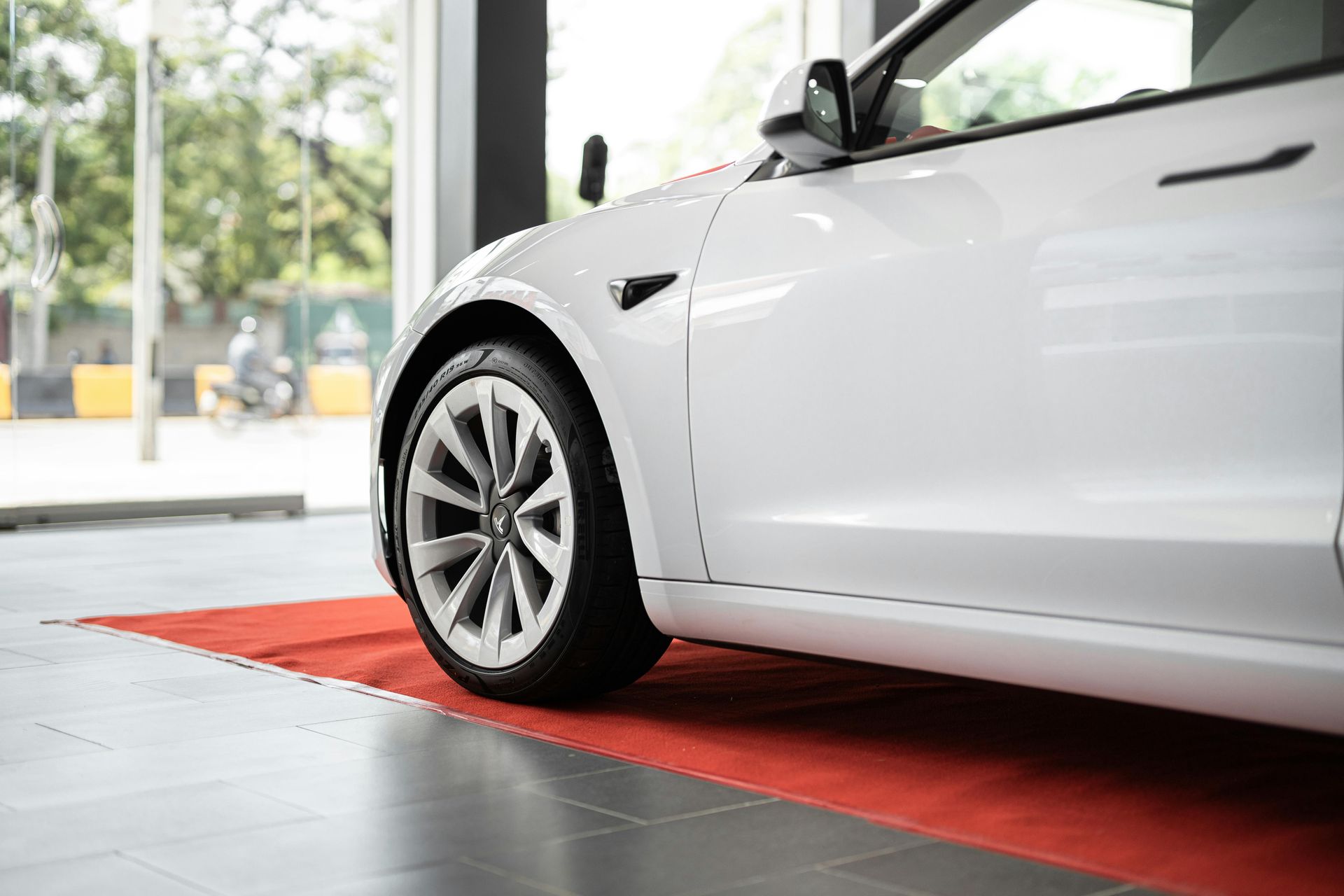 A white tesla model 3 is parked in a showroom on a red carpet.