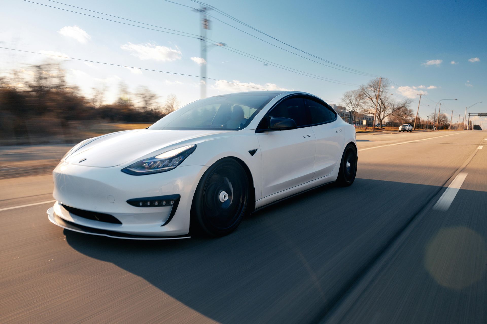 A white tesla model 3 is driving down a road.