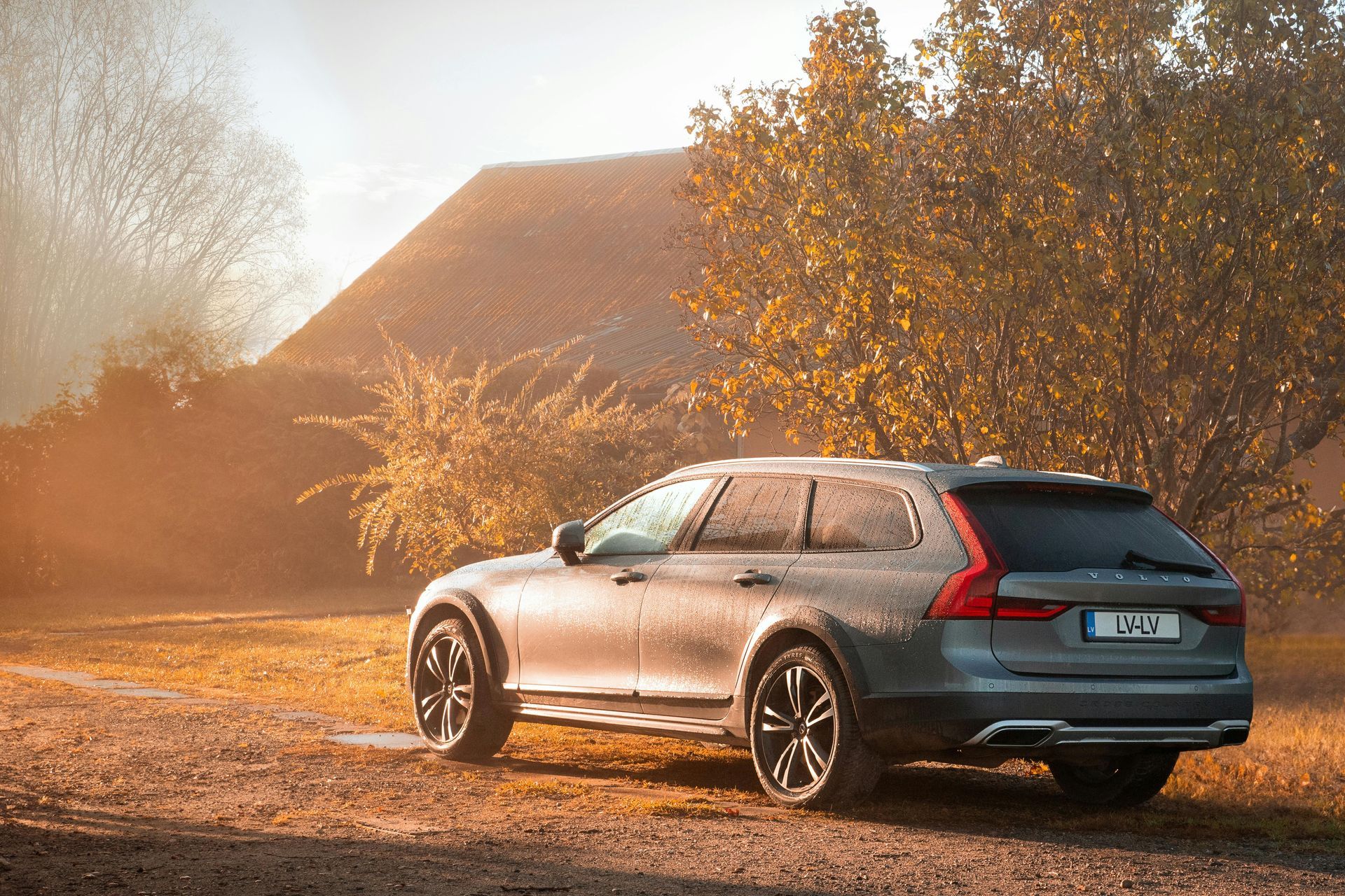 A car is parked in a dirt field in front of a house.