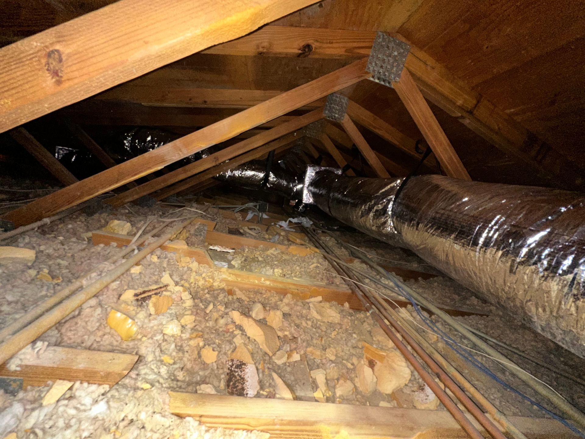 Care to Cool LLC - Attic interior with wooden rafters, insulation, and a silver HVAC duct.
