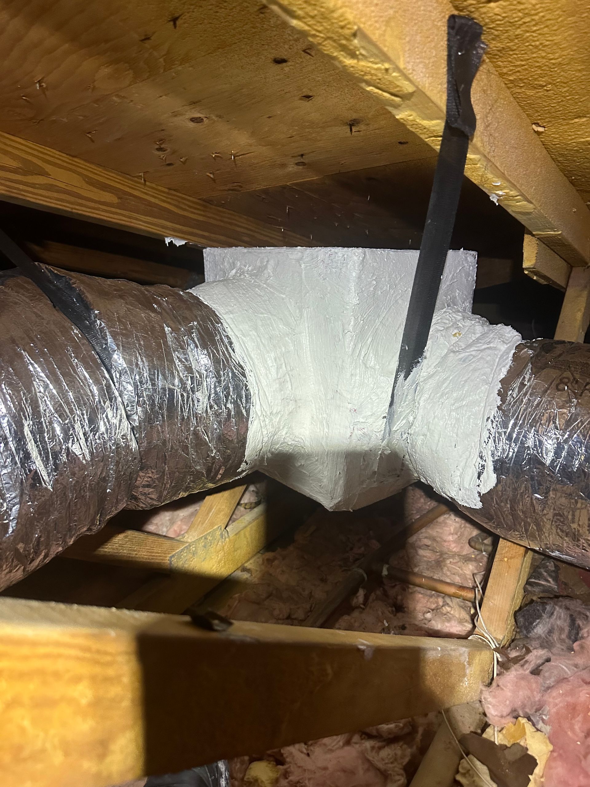 Insulated HVAC duct junction in an attic. The connection is sealed with white spray foam.
