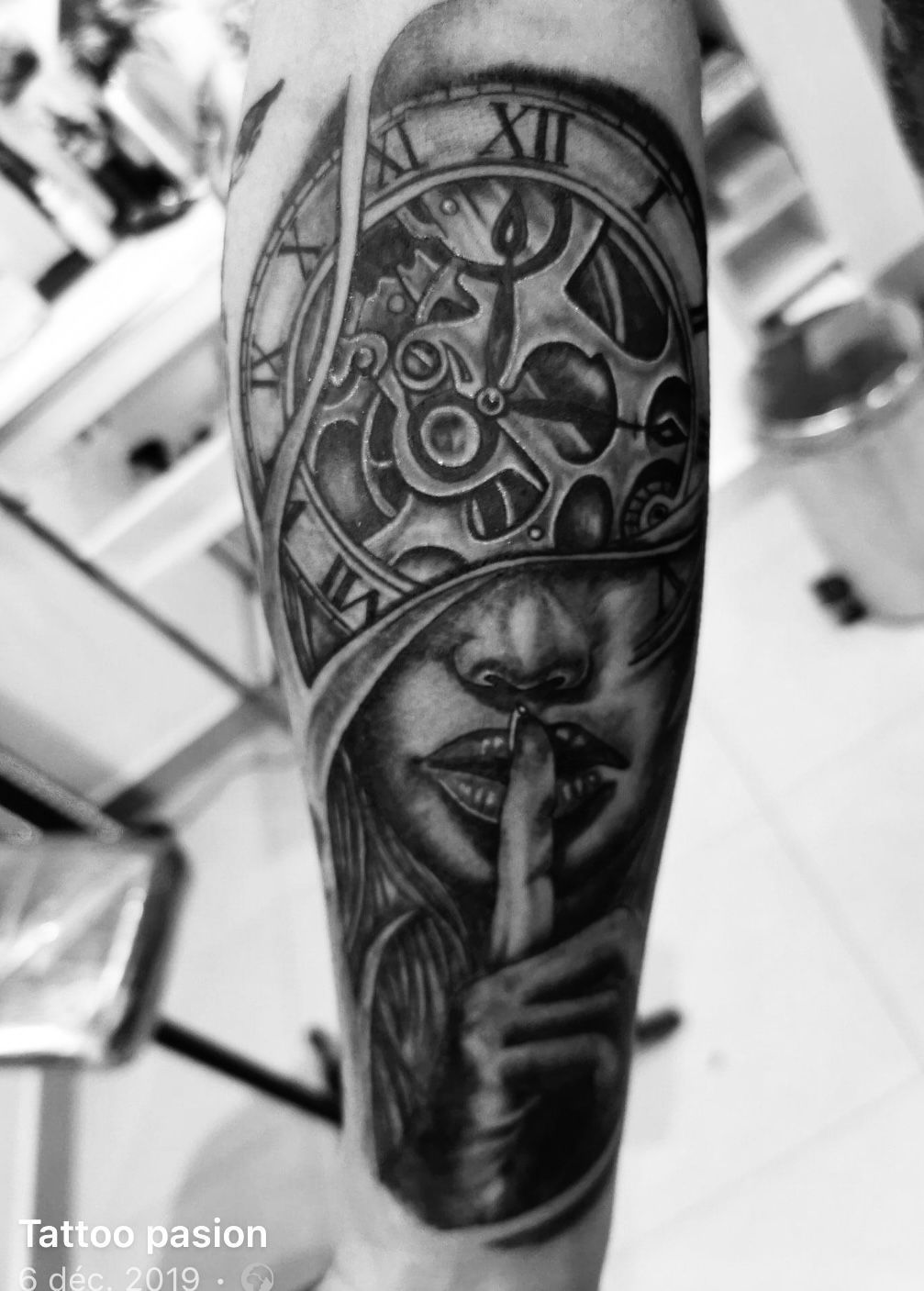 Une photo en noir et blanc d’un tatouage d’une femme avec une horloge sur le visage.