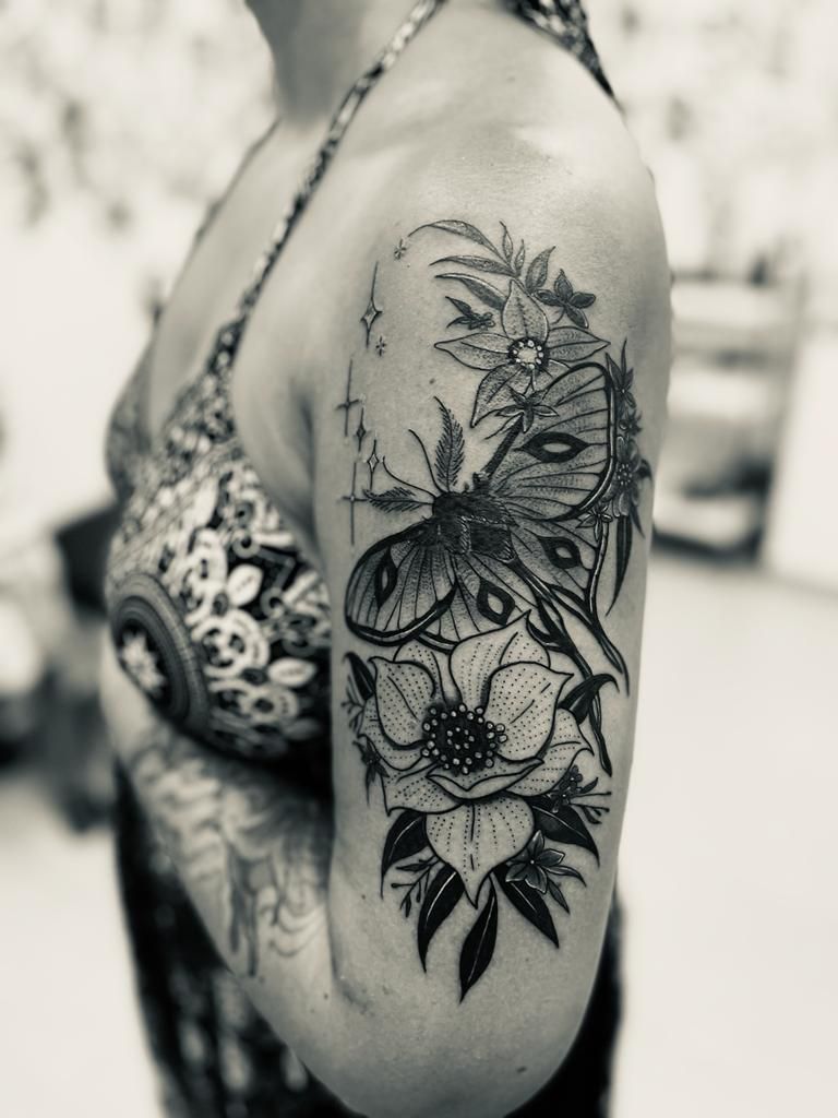 Une femme a un tatouage représentant un papillon et des fleurs sur son bras.