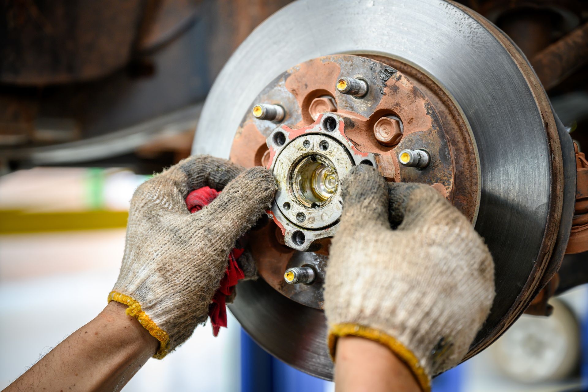 Mechanic's gloved hands working on a car brake rotor in a garage, holding the hub.