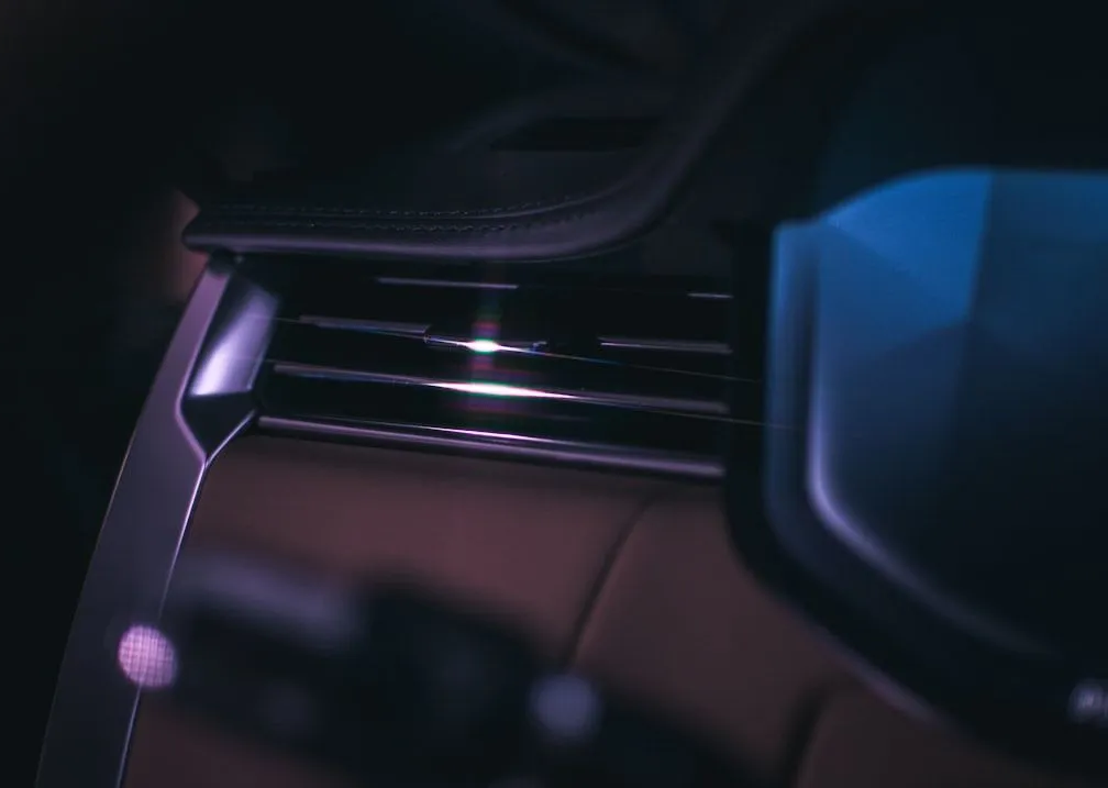 Close-up of a modern car interior dashboard featuring horizontal air vents and brown leather trim in low lighting.