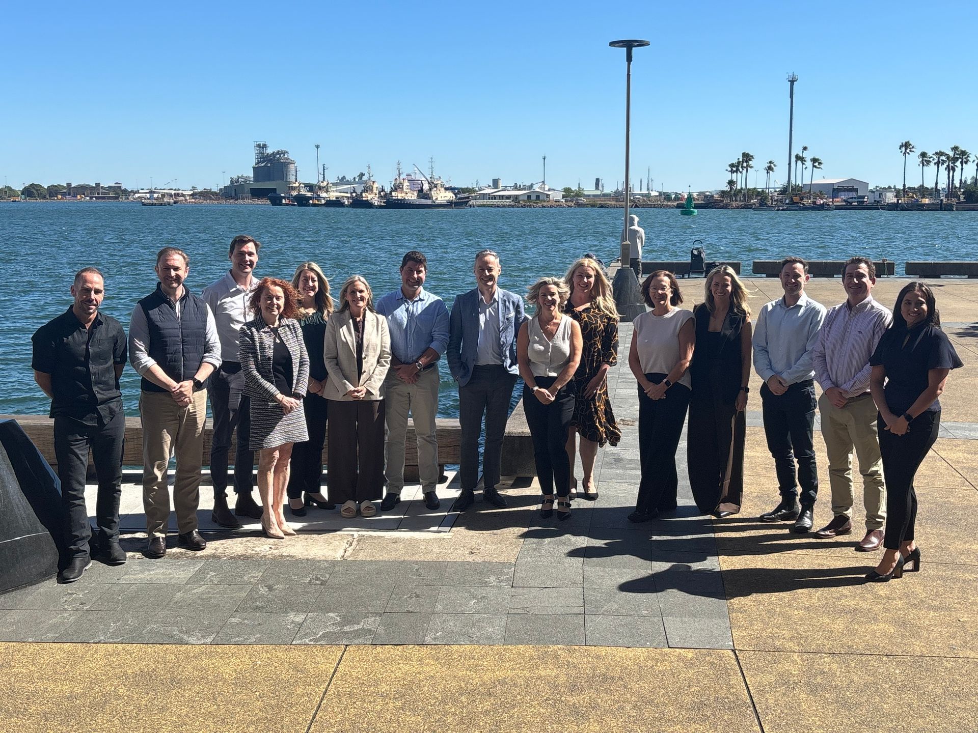 Group of PRP and Alto staff standing on a dock with Newcastle harbour in the background, under a blue sky.