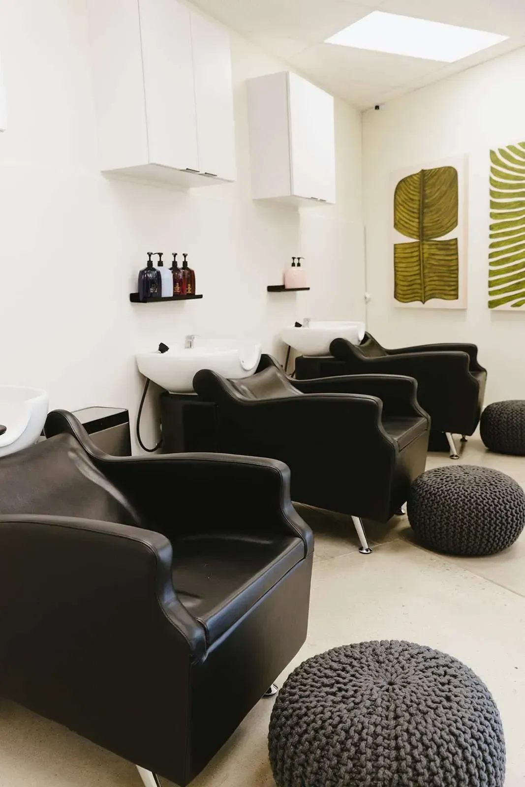 A salon with black chairs and ottomans and a sink.
