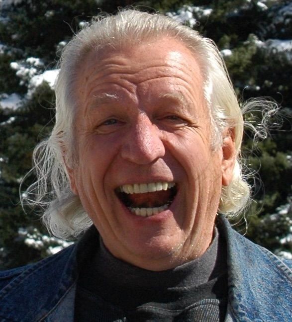 A man with white hair is smiling and wearing a black turtleneck