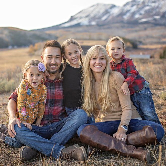 A family is posing for a picture while sitting on the ground in a field.