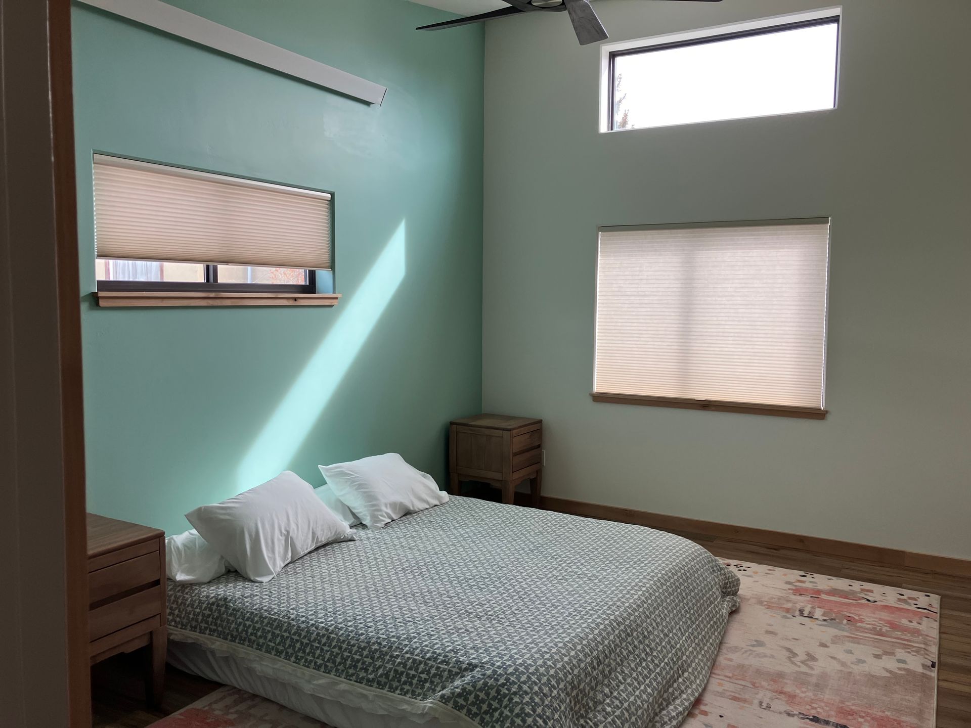 A bedroom with a bed , two windows and a ceiling fan.