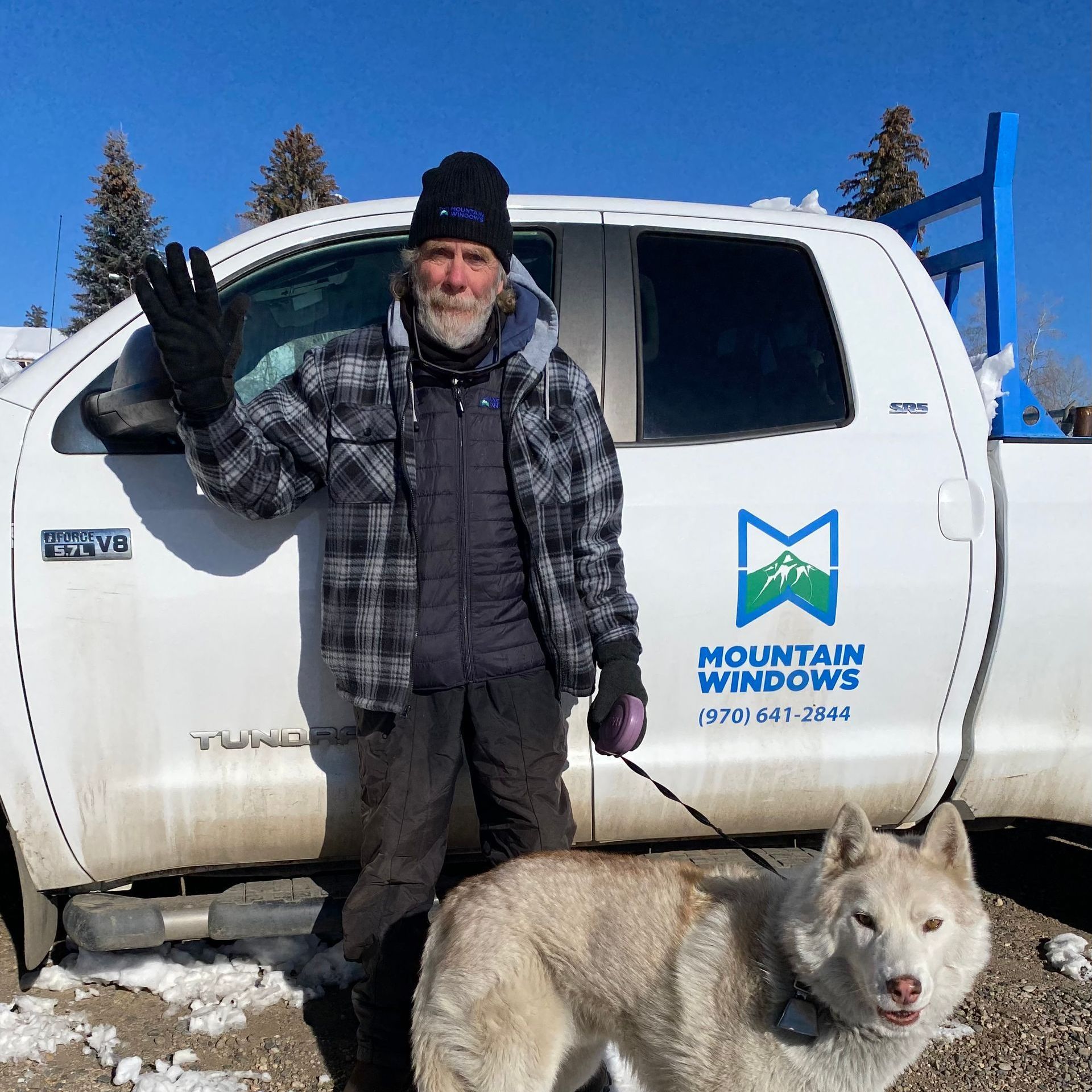 A man standing next to a dog in front of a mountain windows truck