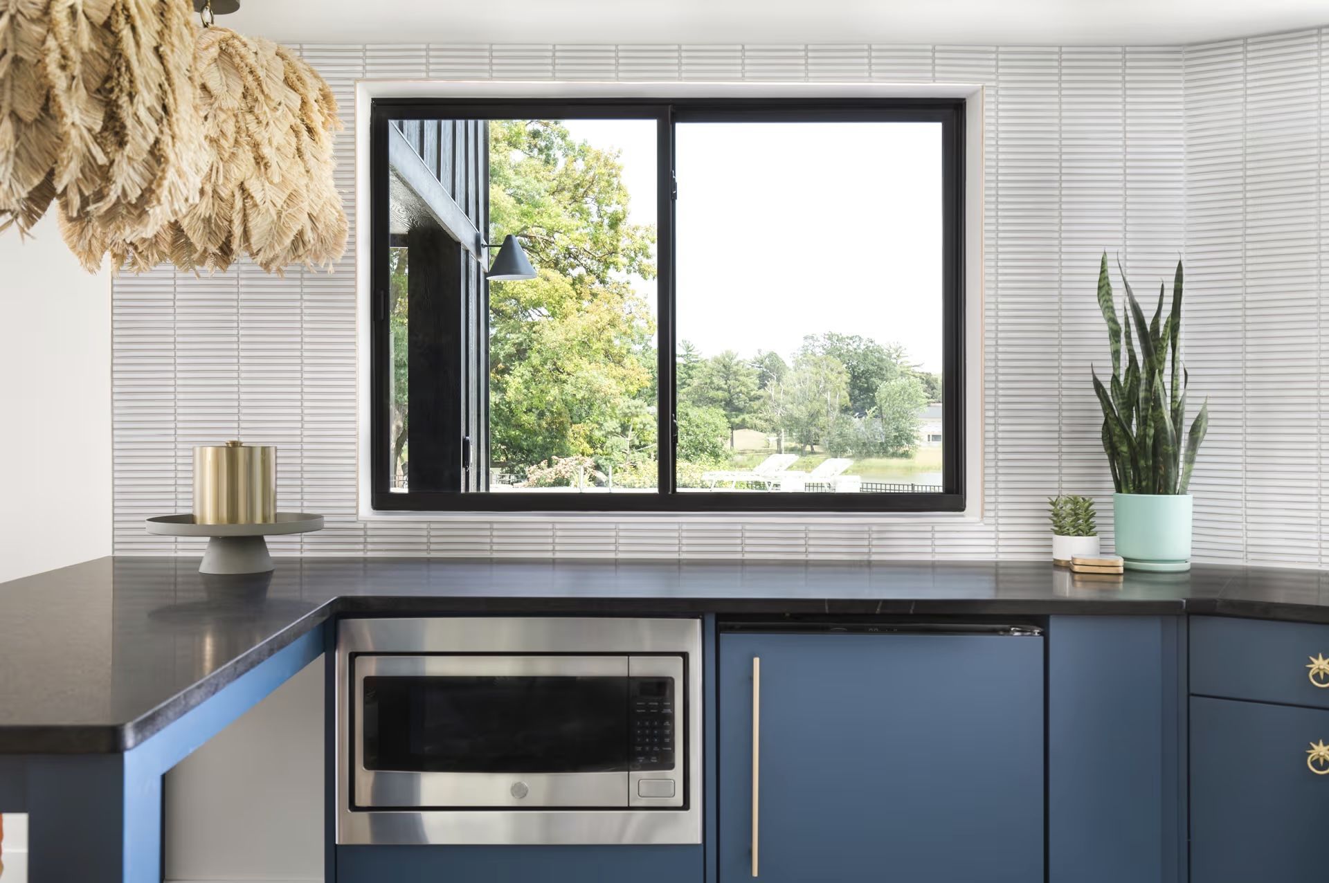 A kitchen with blue cabinets , stainless steel appliances , and a large window.