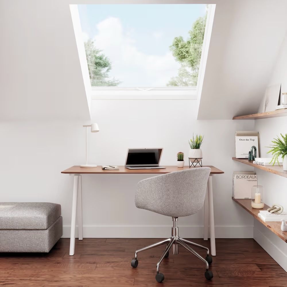 A desk with a chair and a laptop on it in a room with a window.